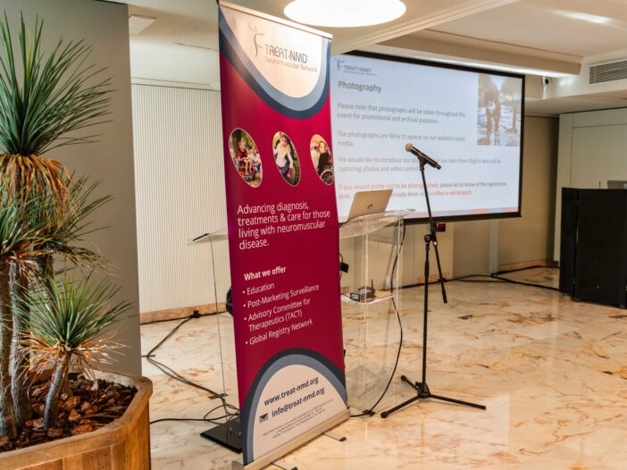 Image shows TREAT-NMD promotional banner next to microphone and screen ready for presentation.